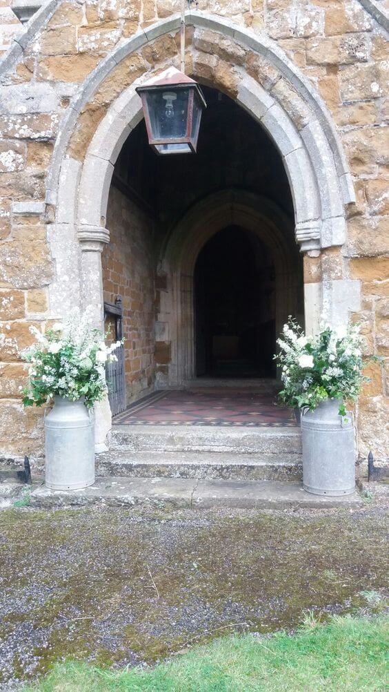 Two cream milk churn flower arrangements outside church entrance